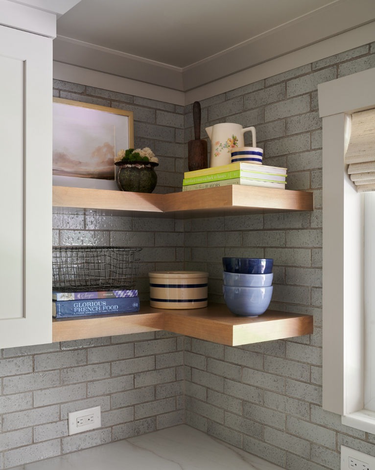<img src="cornerfloatingshelvesinkitchenwithgreybrickbacksplash.png" alt="Light wood floating shelves in corner of kitchen with grey brick backsplash, decorated with bowls, cookbooks, and more">